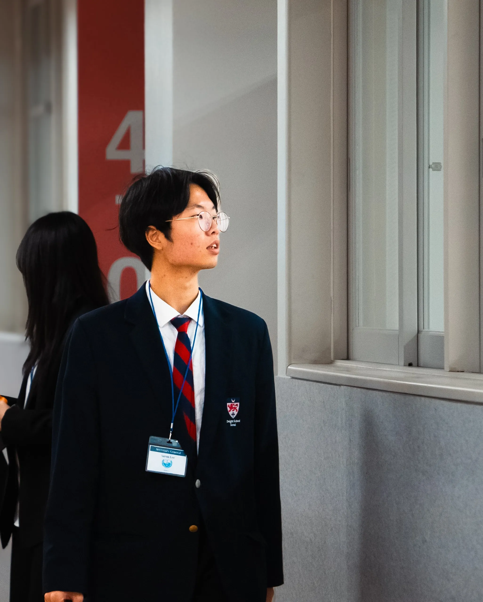 Blazer, tie, lanyard. He looks away from the crowd.