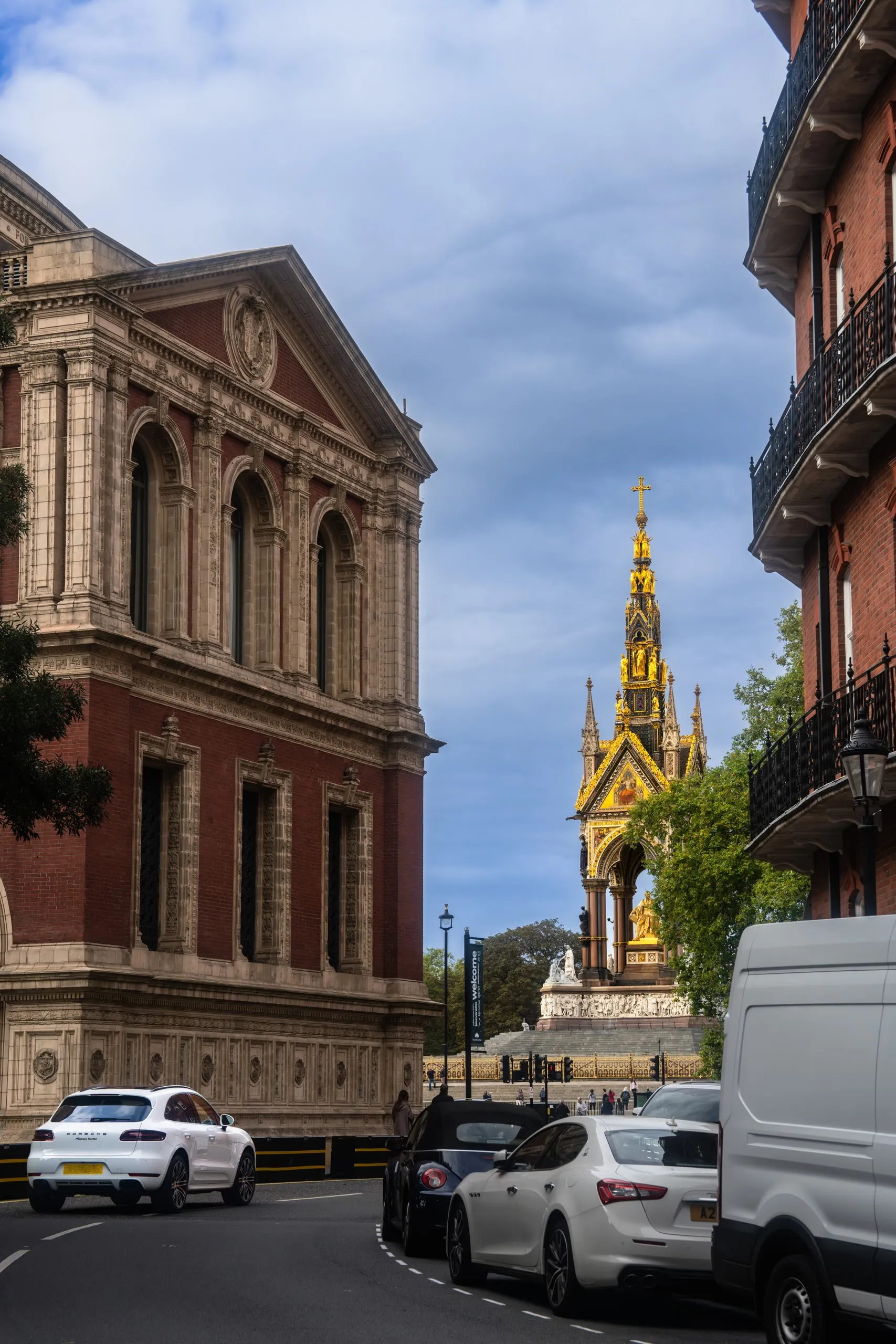 London. The gold spire of the Albert Memorial between two buildings. Everyday traffic below.