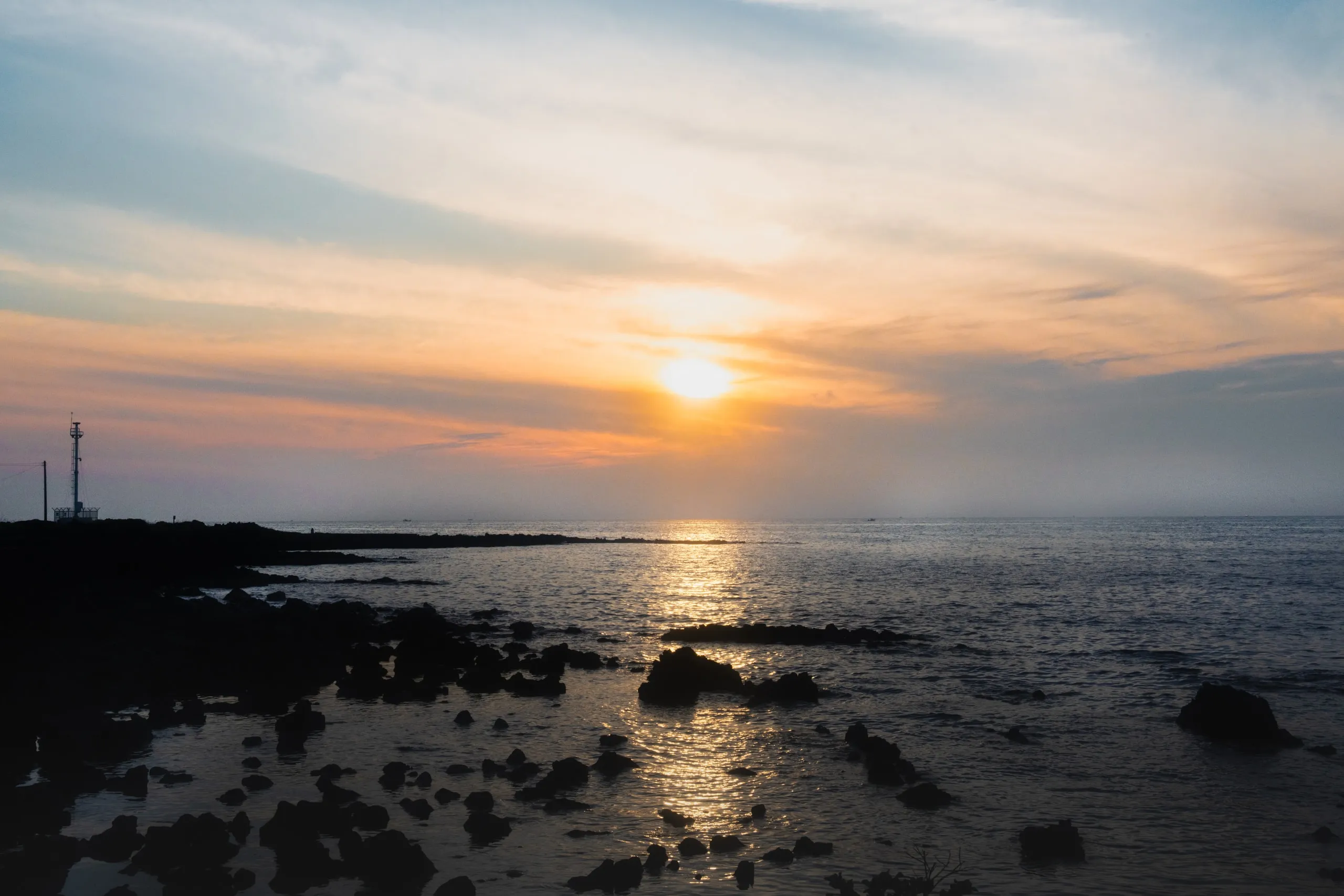 Jeju. The sun going down over black lava rock.
