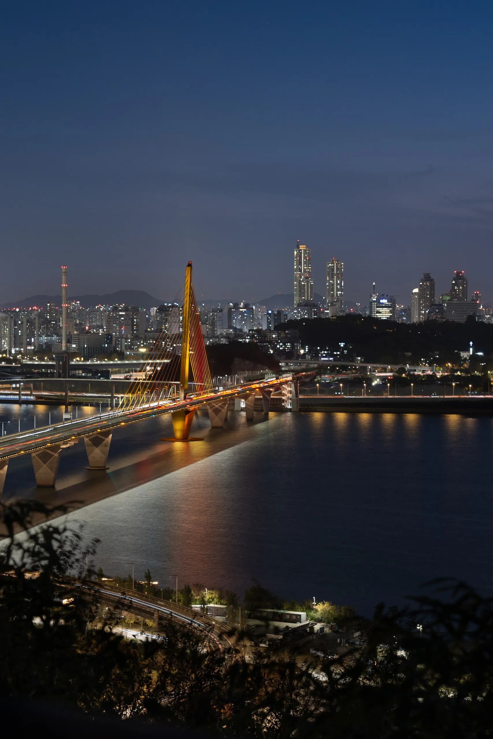 A river city at night. The bridge glows. The towers keep their lights on.