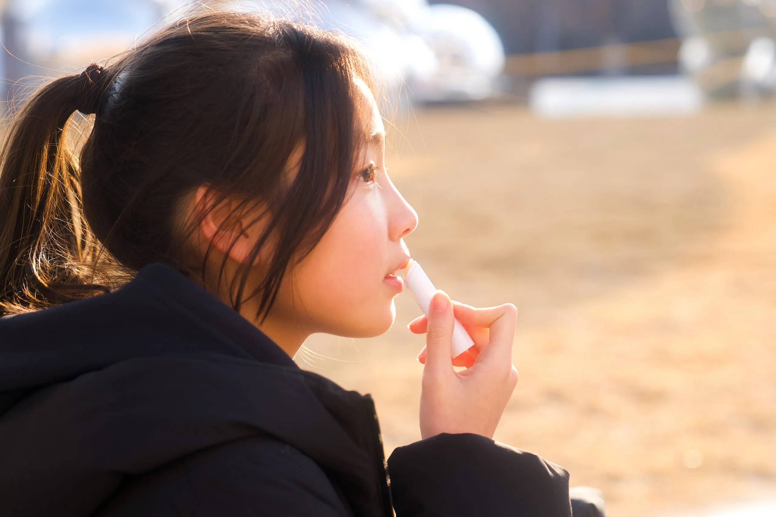 Lip balm in the warm sun. Hair tied back.