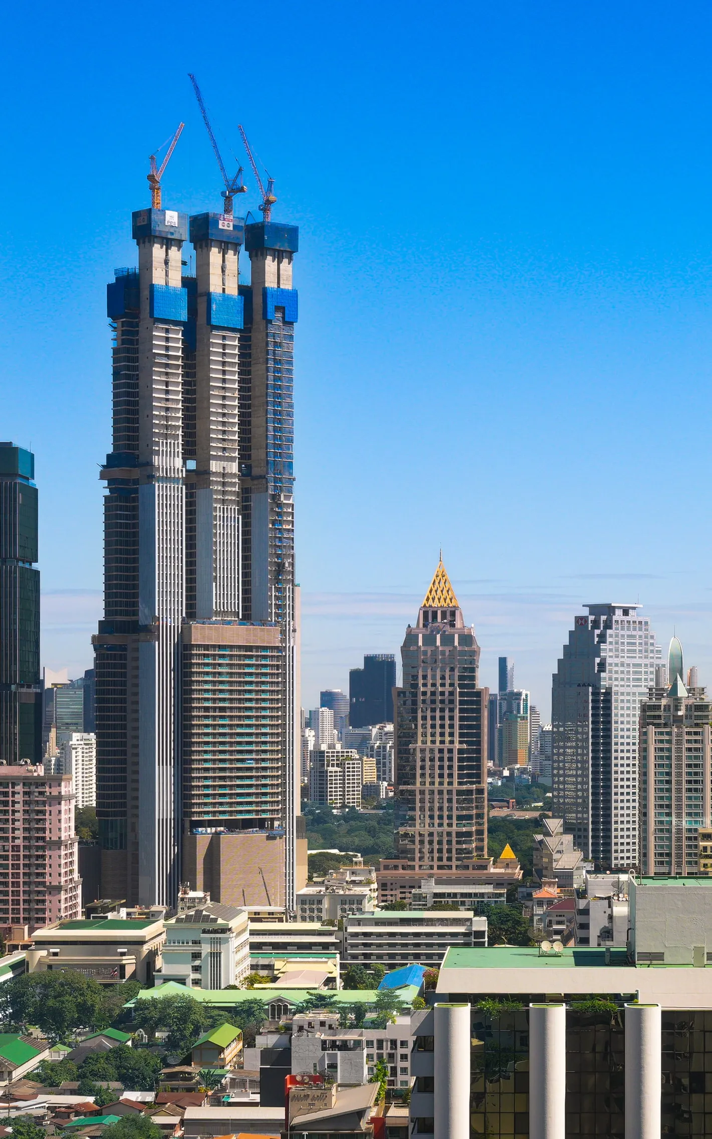A tower still going up, cranes on top. Clear blue sky.