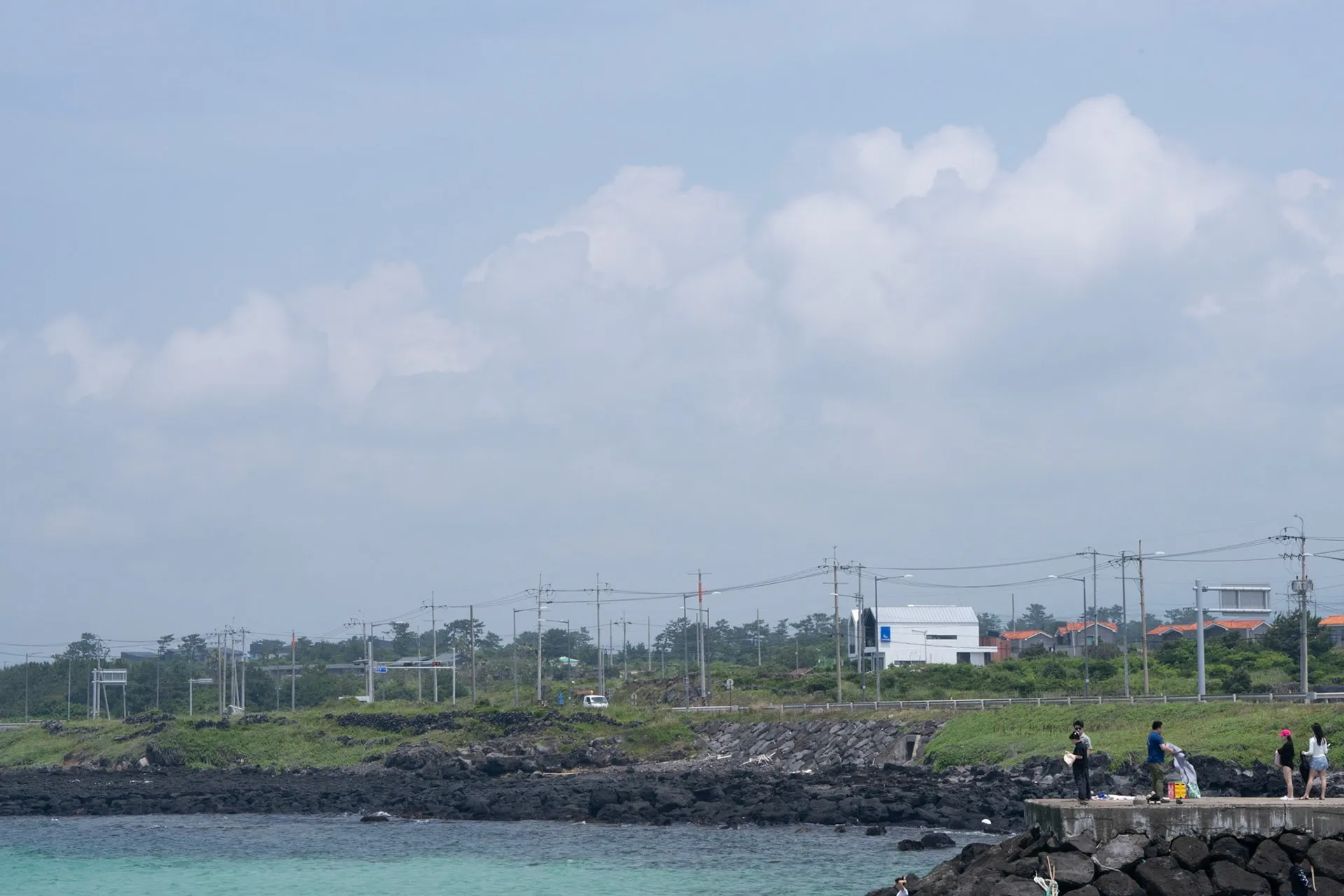 The Jeju coastline. Stone walls, power lines, a white house.